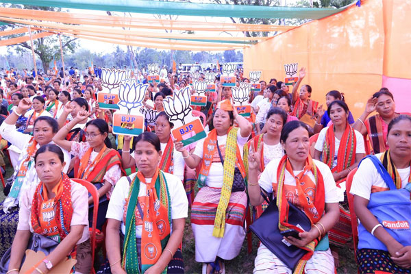 Tripura CM Manik Saha standing in an open-top red vehicle during a BJP roadshow in Bodhjangnagar, surrounded by security personnel and party flags.