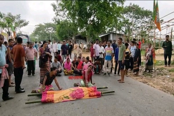 Protesters in Tripura block a road with a victim’s body on a stretcher, surrounded by a crowd and police officers during a conflict over wild elephant attacks.