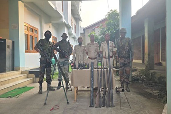 Security personnel stand behind a table displaying seized rifles, improvised mortars, and radio sets in Manipur.