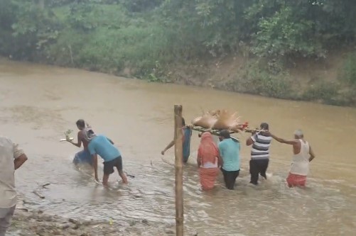 Charilam Villagers wading through river water to carry bodies at the cremation ground for last rites.